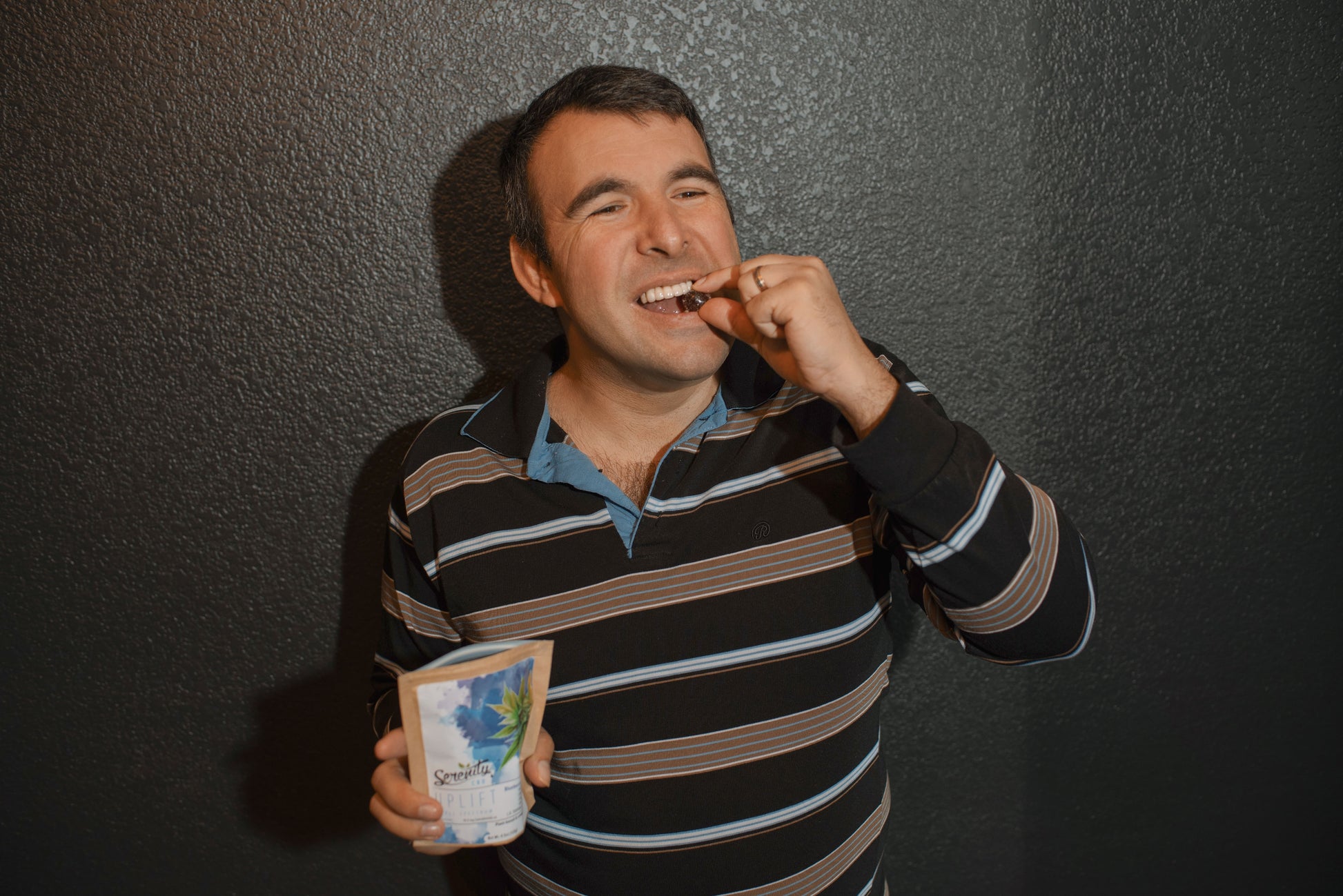 Smiling person enjoying a Serenity CBD ‘Restore’ gummy while holding the pouch—highlighting approachable, everyday recovery and natural wellness support