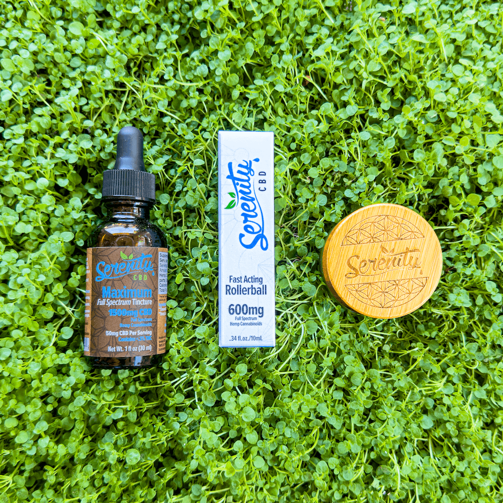 Serenity CBD Maximum Full Spectrum Tincture, Fast Acting 600mg Rollerball, and a wooden Serenity-branded jar arranged on fresh green grass—symbolizing natural relief, balance, and plant-powered wellness