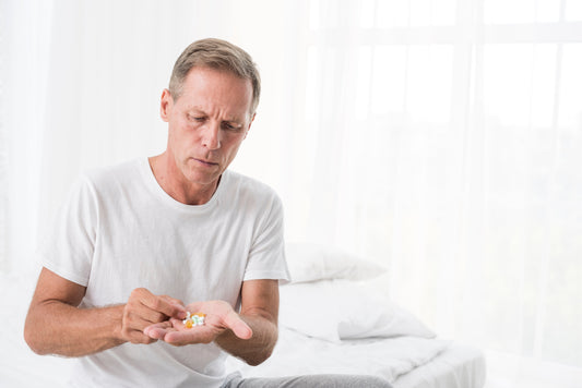 A man sits on his bed, thoughtfully looking at a prescription bottle, considering natural wellness options.