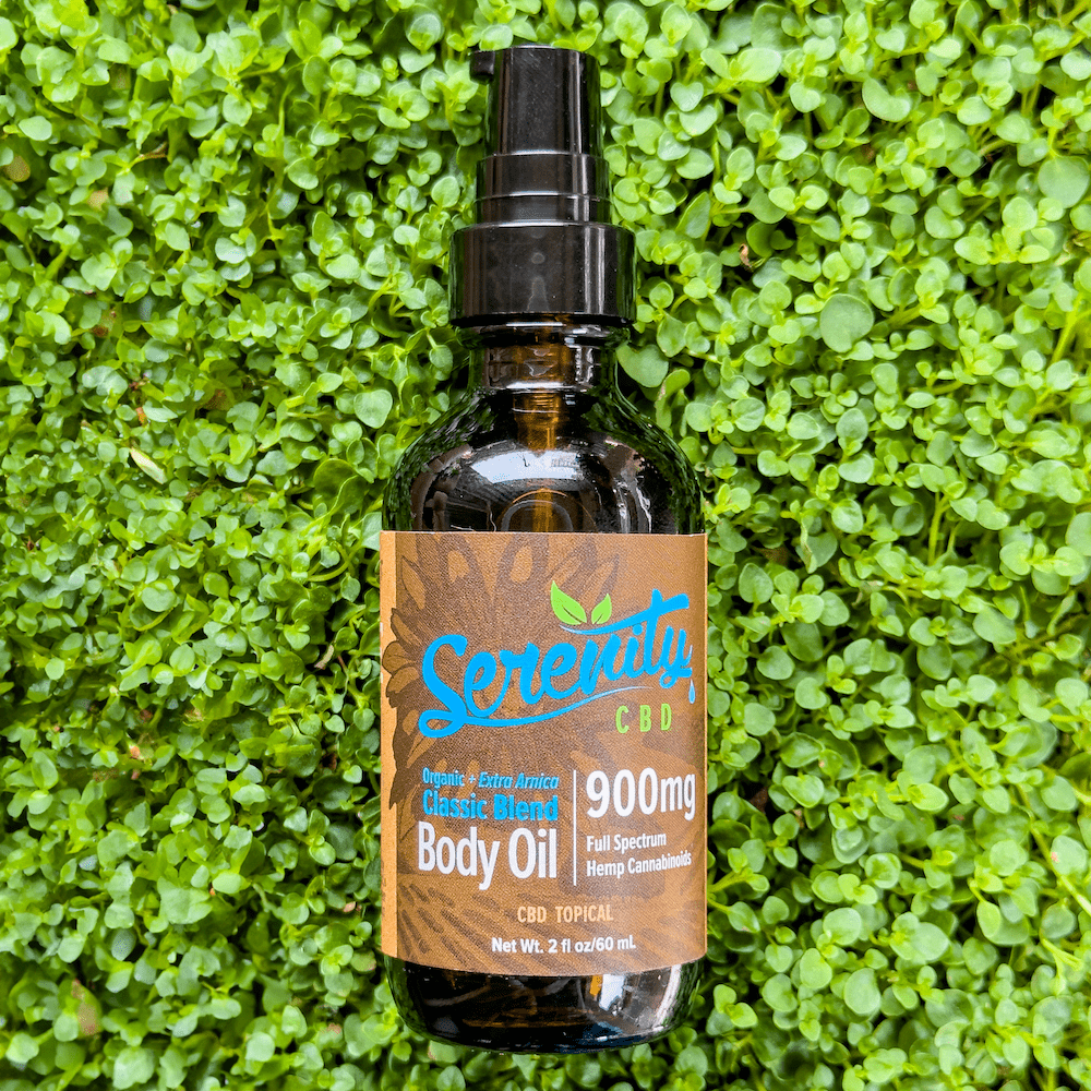 Serenity CBD Body Oil 900mg bottle resting on fresh green grass—evoking natural skincare, soothing relief, and plant-powered nourishment