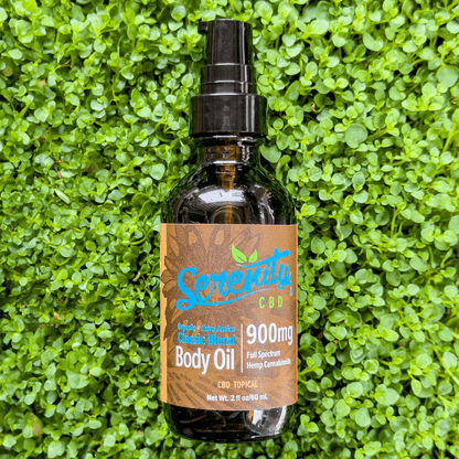 Serenity CBD Body Oil 900mg bottle resting on fresh green grass—evoking natural skincare, soothing relief, and plant-powered nourishment