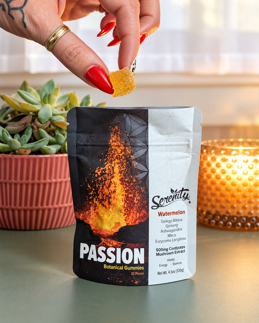 A hand with red nails and a gold ring holds a small yellow gummy above a stand-up pouch of Serenity Passion Watermelon botanical gummies, with a potted succulent and a lit candle in the background.