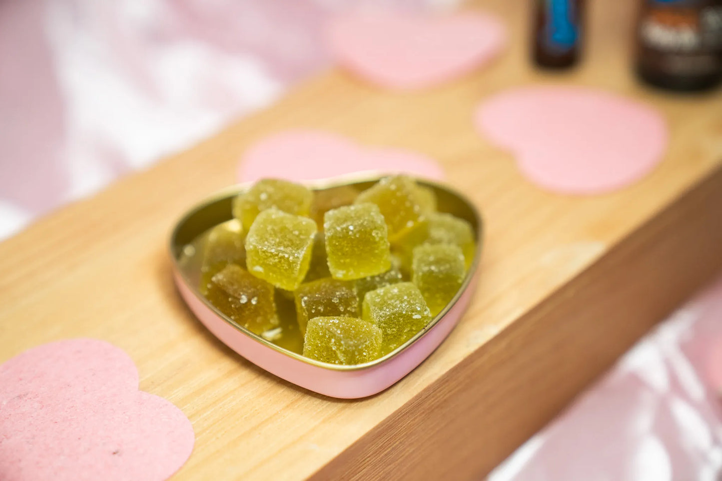Heart-shaped tin filled with green gummies on a wooden surface.