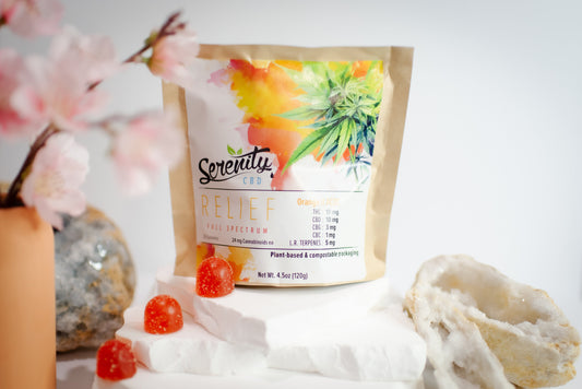 Serenity CBD ‘Relief’ full spectrum gummies pouch displayed with cherry blossoms, crystals, and bright orange gummies—evoking natural harmony, plant-based relief, and mindful wellness