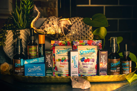 Serenity CBD product collection displayed on a golden tray with a crystal and leafy plants—featuring gummies, tinctures, body oils, topical balms, and rollerballs—symbolizing a holistic approach to natural wellness, relaxation, and balance