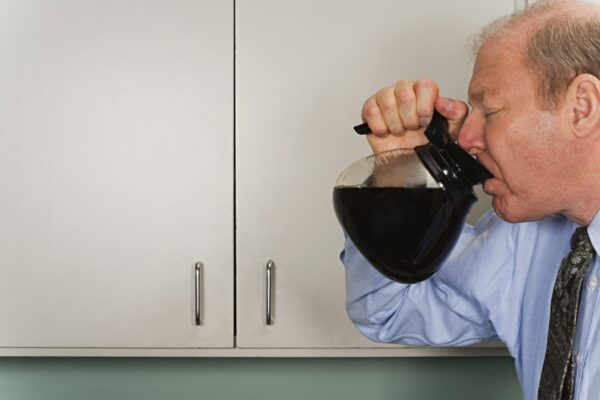 Image of an exhausted businessman in a suit drinking coffee straight from the company pot.