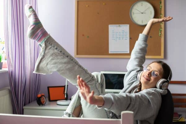 A person is in a serene bedroom setting, engaging in activities that promote a balanced lifestyle and good sleep hygiene. They sit at a desk with a laptop, finishing up work for the day, with a focused yet relaxed expression. Nearby, a yoga mat is laid out, and the person is practicing gentle yoga stretches, preparing their body for rest. The yoga mat is positioned next to an open window, allowing in the soft glow of the setting sun, which adds to the calming atmosphere. The person’s movements are slow and deliberate, indicating a mindful approach to winding down for the evening. This combination of productive work and relaxing physical activity exemplifies a harmonious balance between daily responsibilities and self-care, essential for fostering healthy sleep habits.