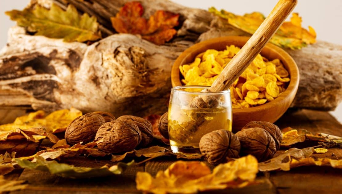 Wooden spoon in a jar of honey surrounded by nuts and autumn leaves, reflecting Ayurvedic fall nutrition and seasonal wellness practices.