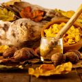 Wooden spoon in a jar of honey surrounded by nuts and autumn leaves, reflecting Ayurvedic fall nutrition and seasonal wellness practices.