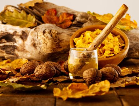 Wooden spoon in a jar of honey surrounded by nuts and autumn leaves, reflecting Ayurvedic fall nutrition and seasonal wellness practices.